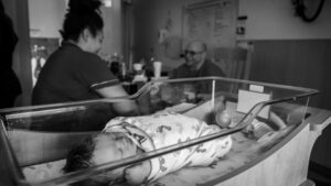 Newborn baby sleeping peacefully in a hospital room, while loving parents sit nearby, talking and sharing joyful laughter."